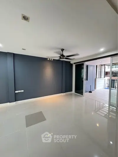 Spacious modern living room with sleek tile flooring and ceiling fan, opening to a balcony with urban views.