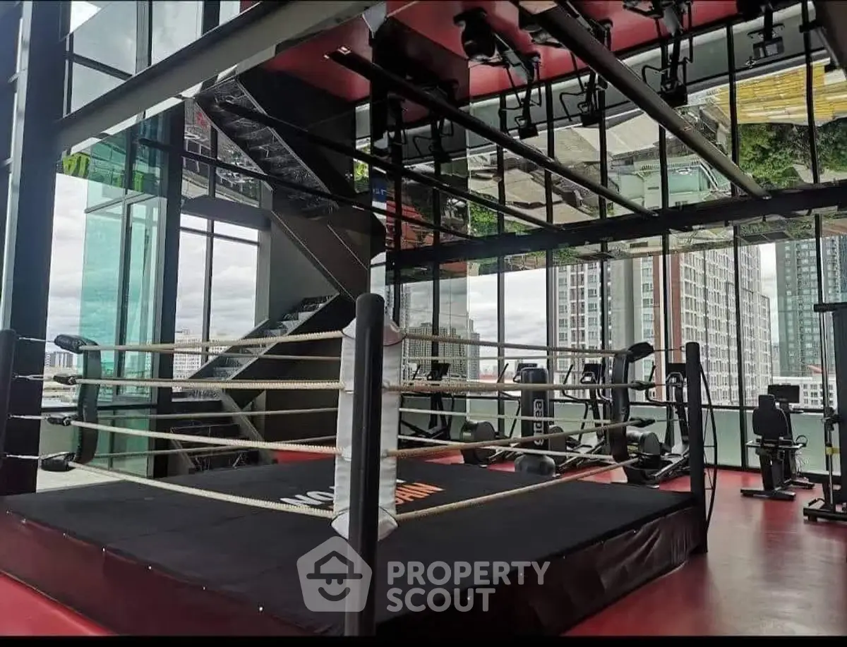Modern gym with boxing ring and city view in luxury high-rise building.