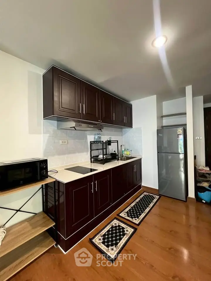 Modern kitchen with dark wood cabinets and stainless steel fridge in a cozy apartment.
