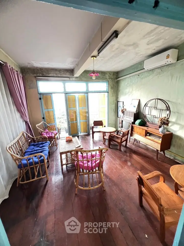 Charming vintage living room with wooden floors, rattan furniture, and large windows for natural light.