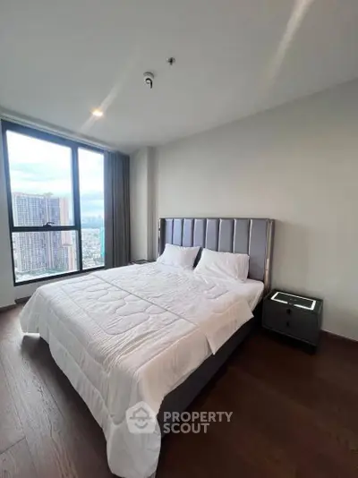Modern bedroom with large window and city view, featuring a stylish bed and sleek nightstand.