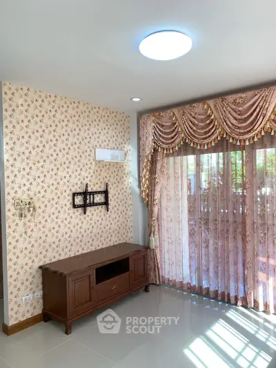 Charming living room with floral curtains and elegant wallpaper, featuring a classic wooden TV stand.