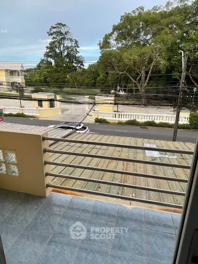 Charming balcony view overlooking a serene street and lush greenery, perfect for relaxation.