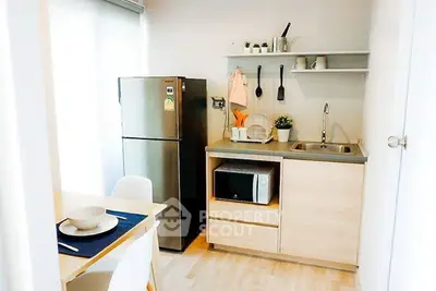 Modern compact kitchen with stainless steel fridge and microwave in cozy apartment.