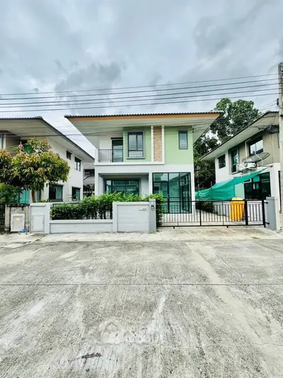 Modern two-story house with green facade and spacious driveway in suburban neighborhood.