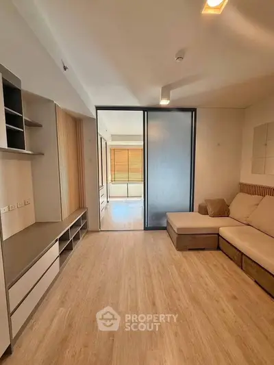 Modern living room with wooden flooring and sliding glass doors leading to a bright adjacent room.