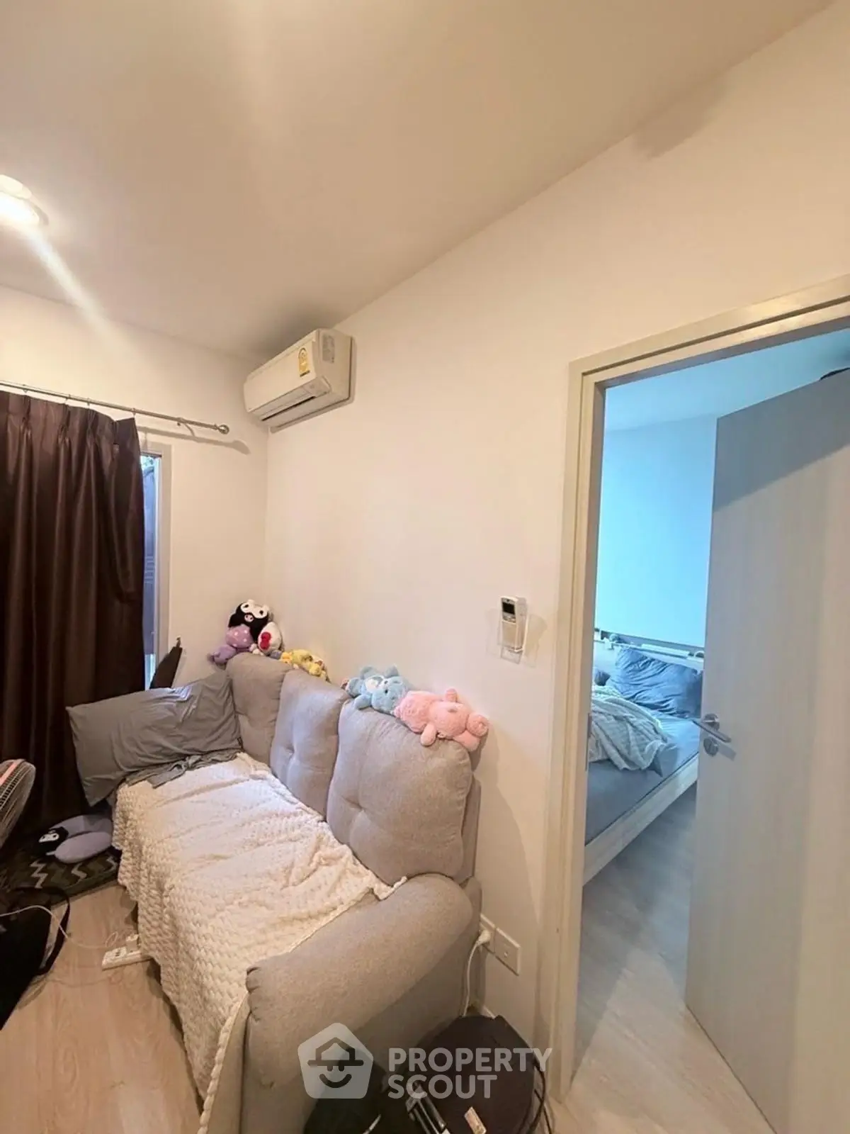 Cozy living room with plush sofa and air conditioning, adjacent to a bright bedroom.