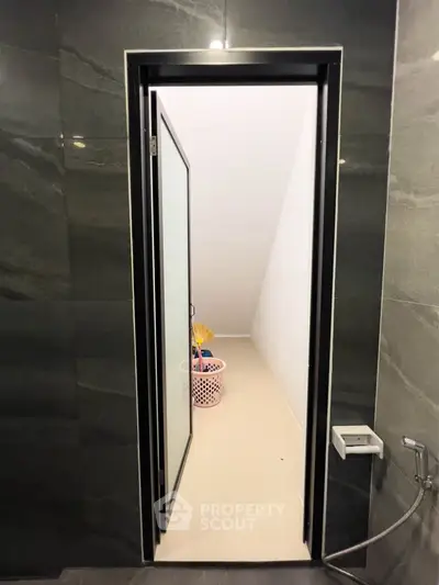 Modern bathroom with sleek black tiles and a frosted glass door leading to a storage area.