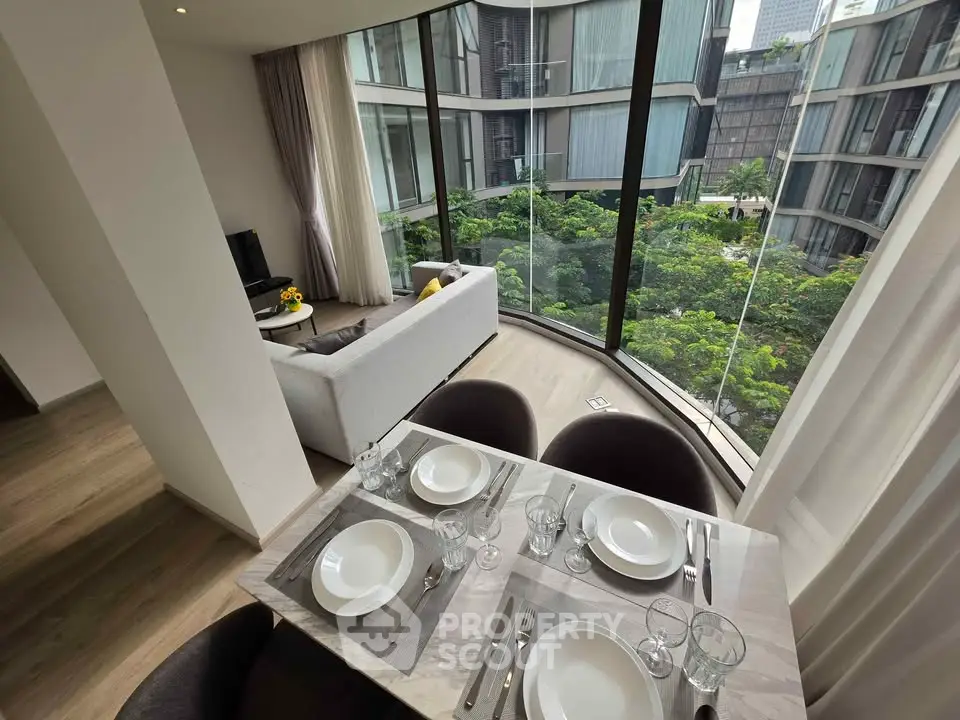 Modern living room with dining area and large windows offering lush green views in a luxury apartment.