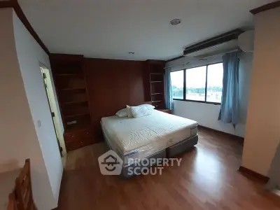 Spacious bedroom with large window and wooden flooring in modern apartment