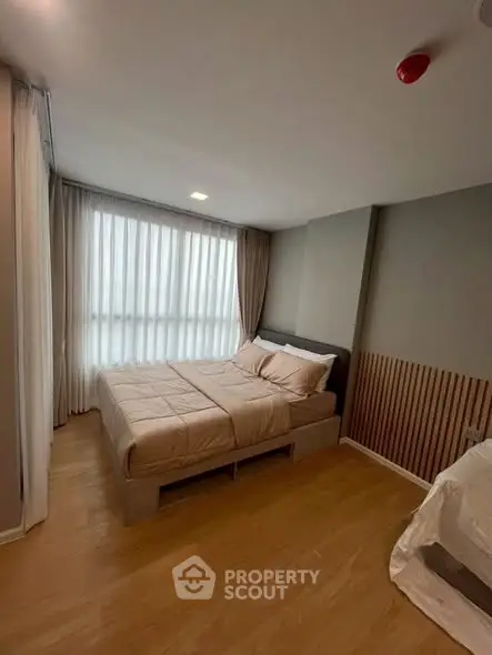 Modern bedroom with cozy bed and natural light through large window, featuring elegant wood flooring.