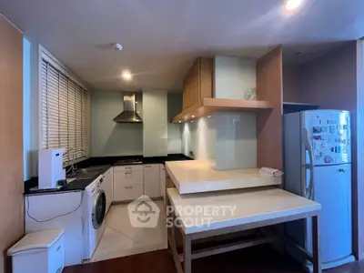 Modern kitchen with sleek appliances and open layout, featuring washing machine and fridge.