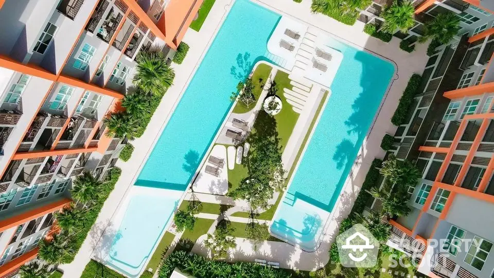 Stunning aerial view of modern apartment complex with large swimming pool and lush greenery.