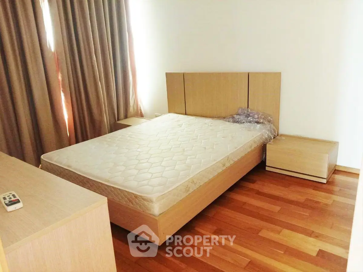 Spacious bedroom with wooden flooring and modern furniture in a bright apartment.
