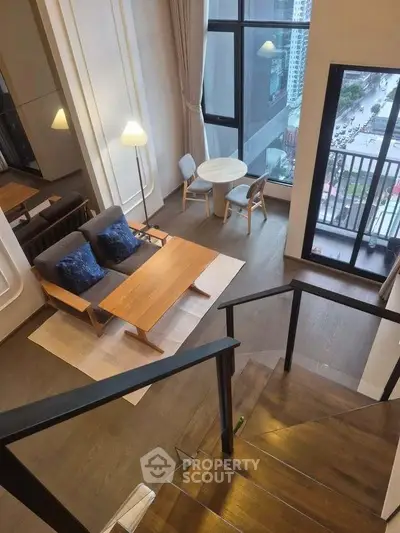 Modern duplex living room with large windows and city view, featuring stylish furniture and a cozy atmosphere.