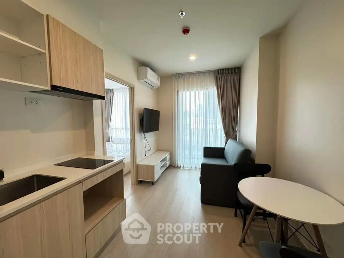 Modern living room with open kitchen, cozy sofa, and natural light from large window.