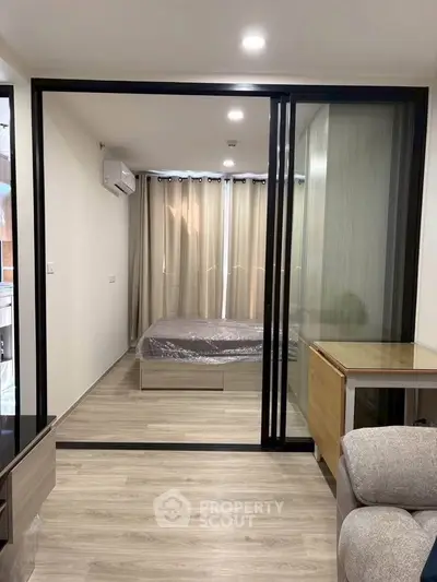 Modern studio apartment with sliding glass doors separating bedroom and living area, featuring sleek wooden flooring.