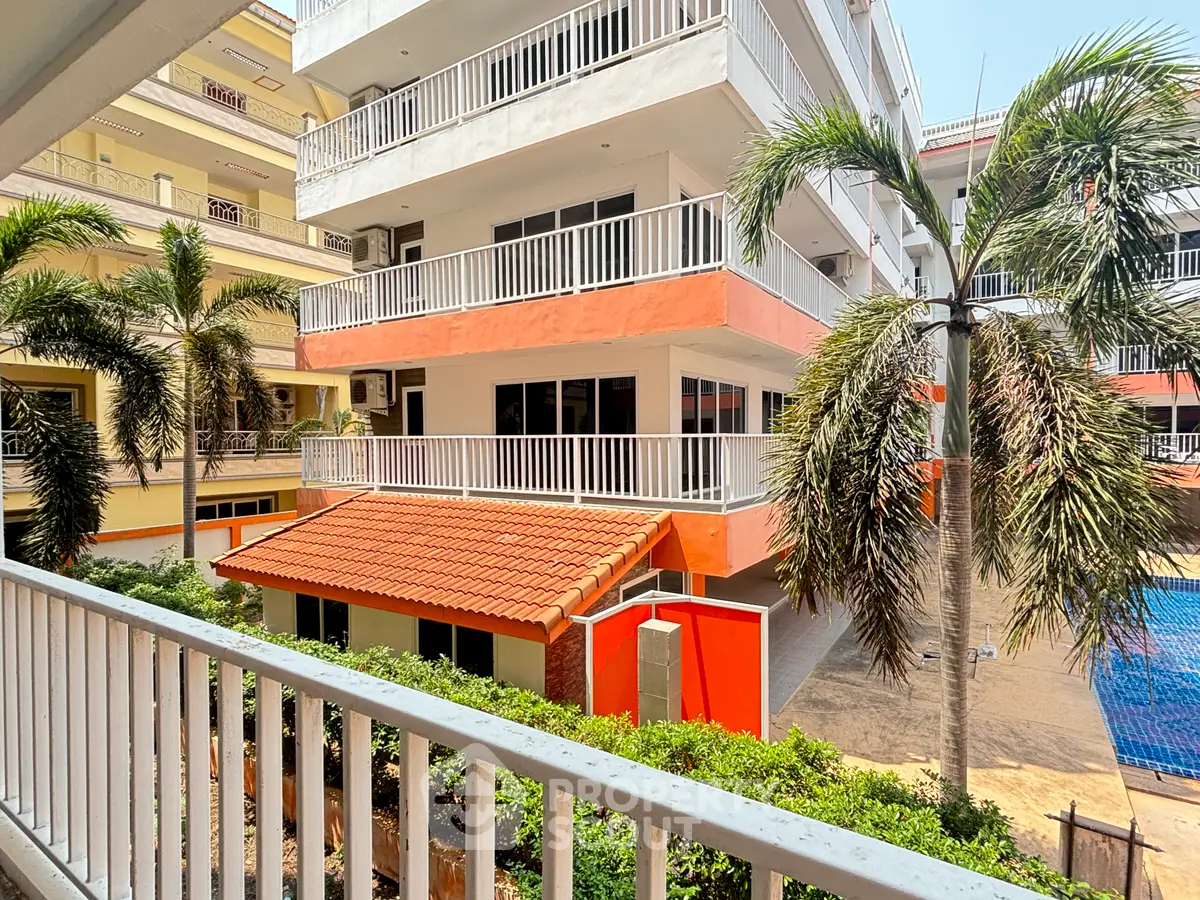 Modern apartment building with balconies and palm trees, featuring a vibrant orange facade and poolside view.