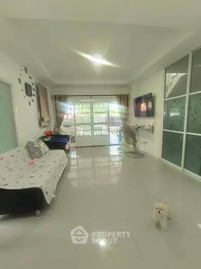 Spacious living room with modern decor and natural light, featuring a cozy sofa and wall-mounted TV.