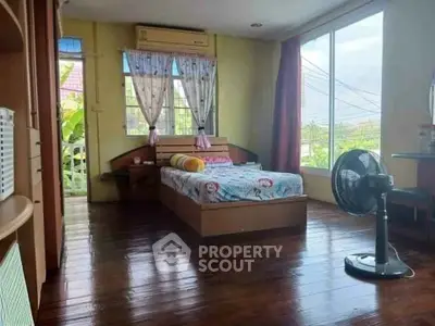 Spacious bedroom with wooden flooring and large windows offering natural light and garden view.