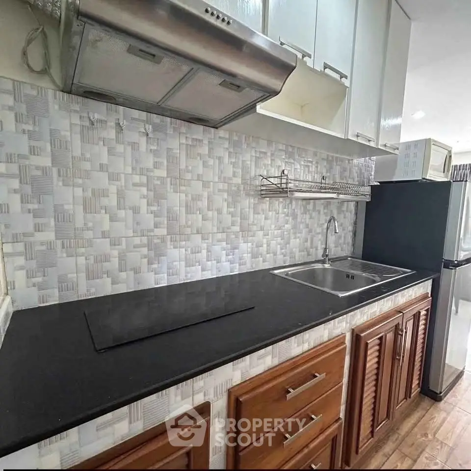 Modern kitchen with sleek black countertop and stylish backsplash in a contemporary apartment.