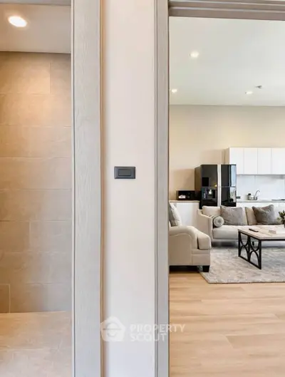 Modern open-plan living room with stylish furniture and kitchen area, featuring neutral tones and sleek design.