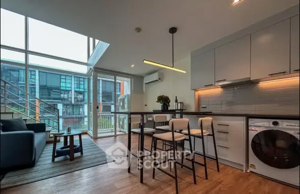 Modern open-plan living area with kitchen and large windows in contemporary apartment.