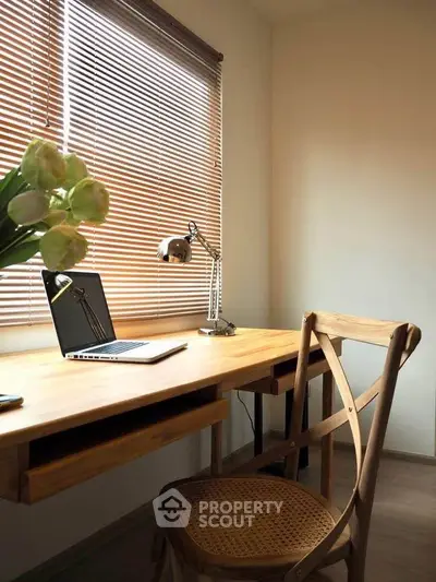 Cozy study room with wooden desk, chair, and natural light from window blinds.
