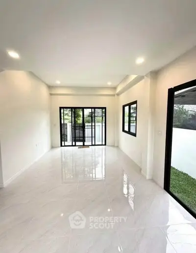 Spacious modern living room with large windows and glossy tiled floor, offering abundant natural light.