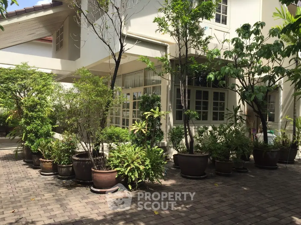 Charming exterior view of a house with lush greenery and potted plants on a paved driveway.