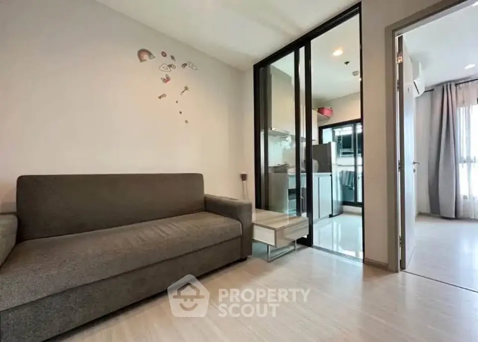 Modern living room with sleek sofa and glass partition leading to a bright kitchen area.