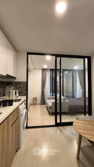 Modern open-layout apartment with sleek kitchen and cozy living area, featuring a sliding glass partition to the bedroom.