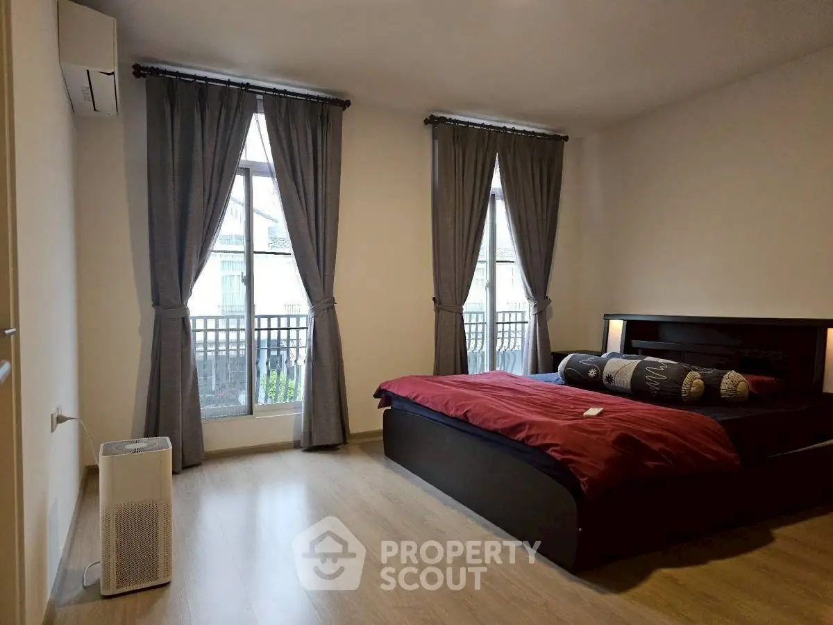Spacious bedroom with large windows and elegant curtains, featuring a modern bed and hardwood flooring.