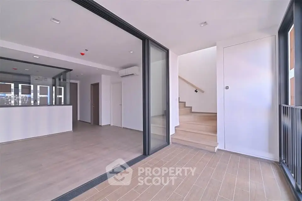 Spacious modern interior with open layout and wooden flooring, featuring large windows and a staircase.