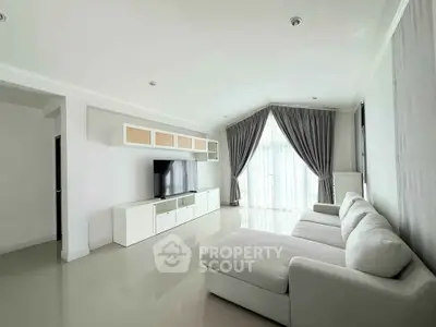 Spacious modern living room with sleek white furniture and large windows for natural light.