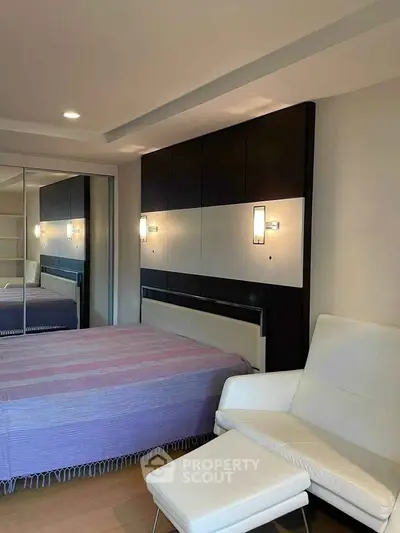 Modern bedroom with stylish lighting and mirrored closet doors, featuring a cozy chair and sleek design.