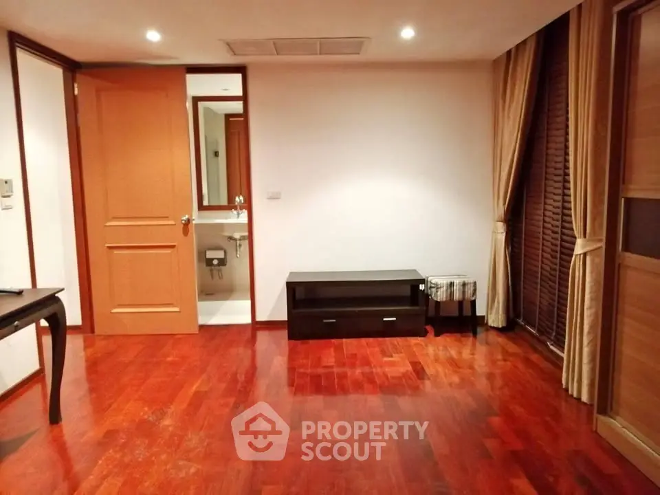 Spacious room with wooden flooring and elegant curtains, featuring a small bathroom entrance.