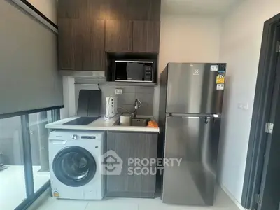 Modern kitchen with washing machine, microwave, and stainless steel fridge in compact layout.