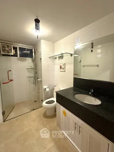 Modern bathroom with glass shower and sleek vanity in contemporary apartment.