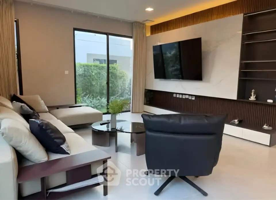 Modern living room with sleek furniture and large TV, featuring a garden view through glass doors.