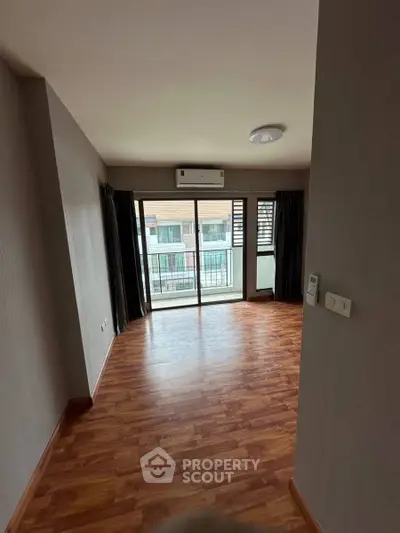 Spacious living room with wooden flooring and balcony access in modern apartment.