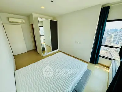 Modern bedroom with large window offering city view, featuring minimalist decor and mirrored wardrobe.