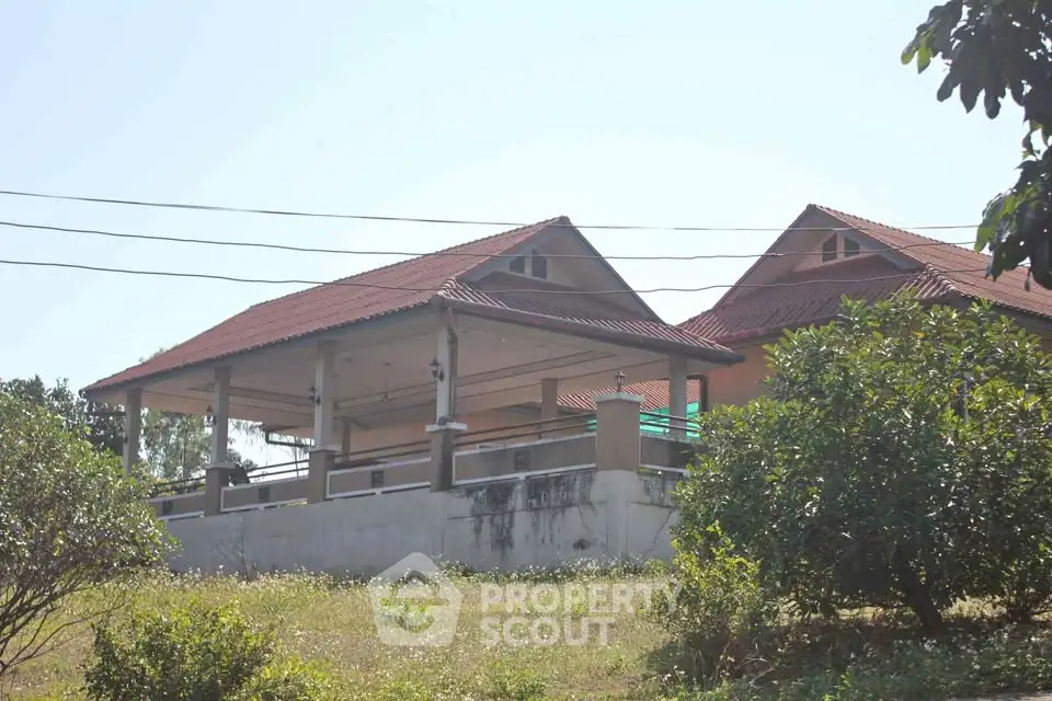 Charming hillside home with red-tiled roof and spacious veranda, surrounded by lush greenery.