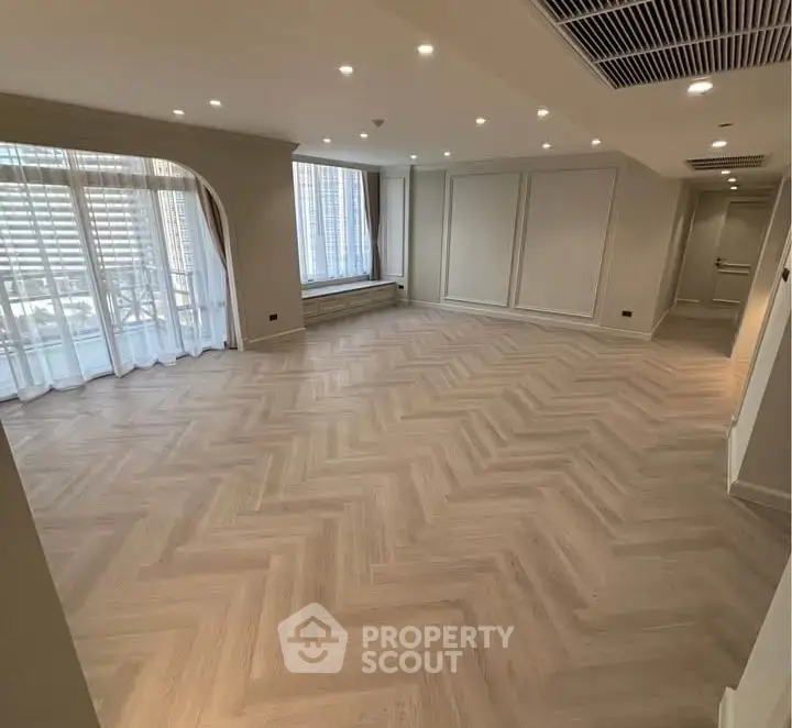 Spacious modern living room with elegant herringbone flooring and large windows.