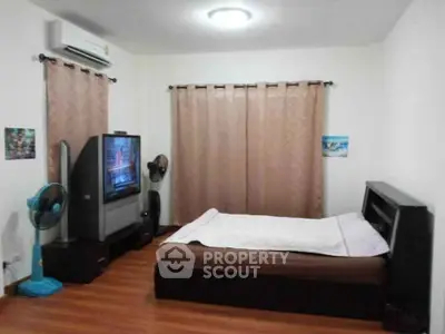 Cozy bedroom with wooden flooring, TV, and air conditioning, perfect for relaxation.