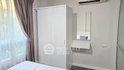 Cozy bedroom with white wardrobe and wall-mounted mirror, featuring soft natural light through curtains.