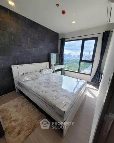 Modern bedroom with city view, featuring a stylish bed and large window overlooking a lush park.