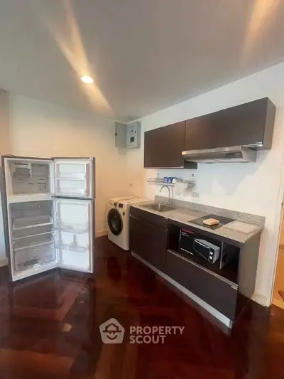 Modern kitchen with open fridge, washing machine, and microwave on sleek wooden flooring.