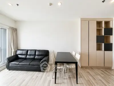 Modern living room with sleek black sofa and dining area in open layout apartment.