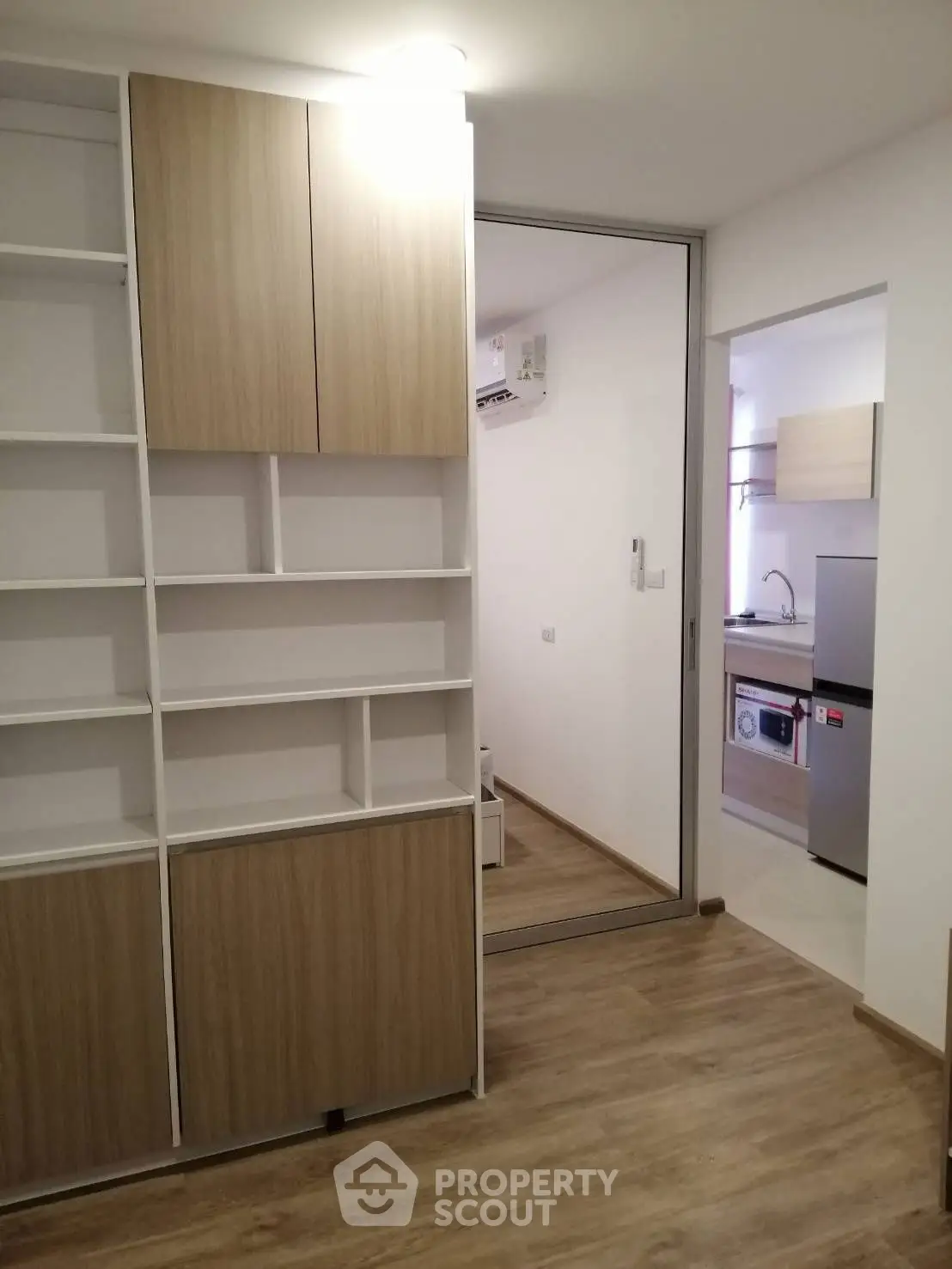 Modern apartment with sleek kitchen and stylish wooden flooring, featuring built-in shelving for optimal storage.